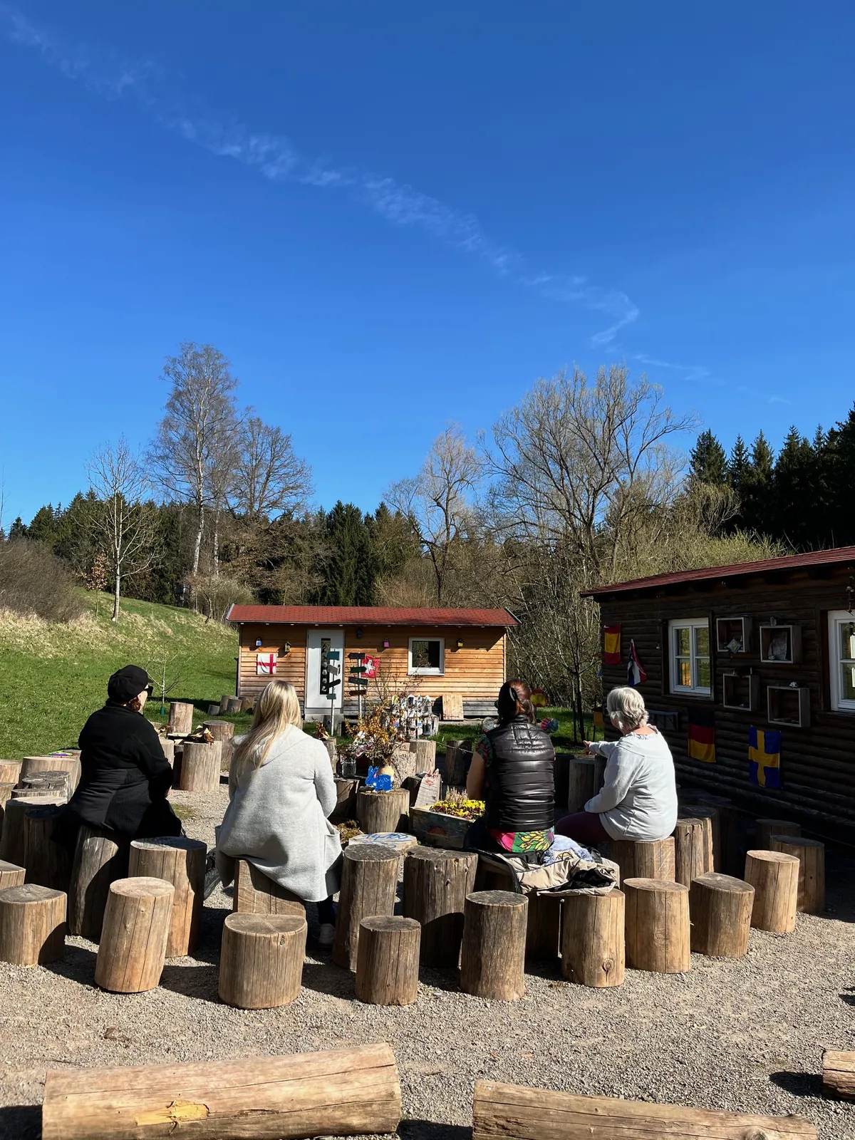 Teilnehmende sitzen auf Holzstämmen vor dem Atelier im Grünen