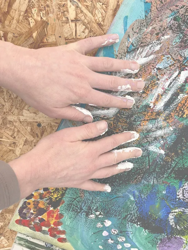Hände streichen weiße Farbe über eine bunte Leinwand